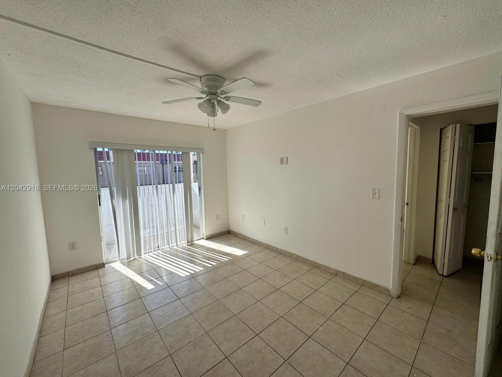An empty room features white walls, light-colored tile flooring, a ceiling fan, and sliding glass doors — 6675 W 4th Ave # 310, Hialeah FL 33012, HIALEAH, FL