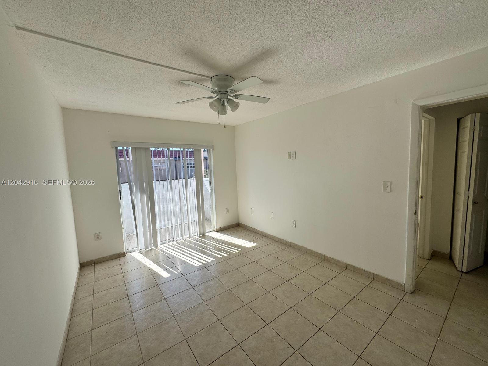 An empty room features white walls, tile flooring, a ceiling fan, and sliding glass doors — 6675 W 4th Ave # 310, Hialeah FL 33012, HIALEAH, FL