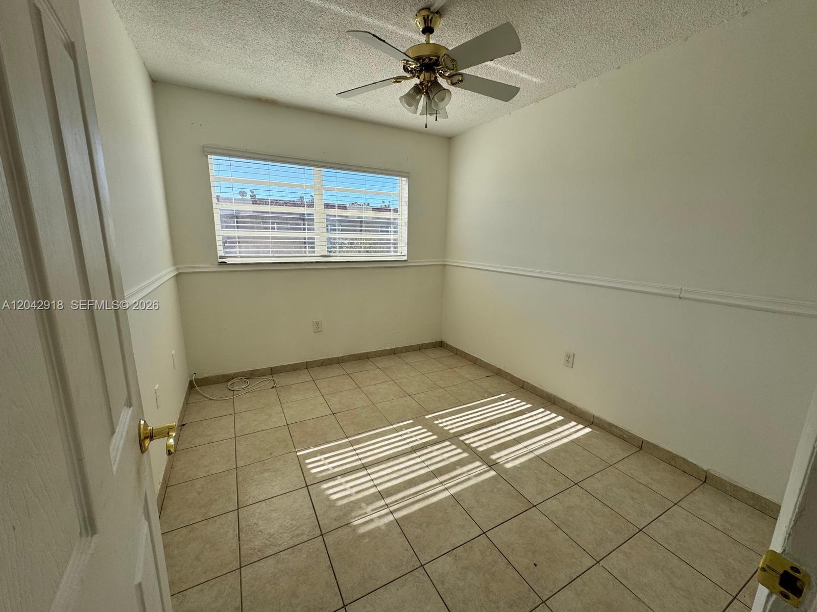 An empty room features beige tile flooring, white walls with chair rail molding, and a ceiling fan — 6675 W 4th Ave # 310, Hialeah FL 33012, HIALEAH, FL