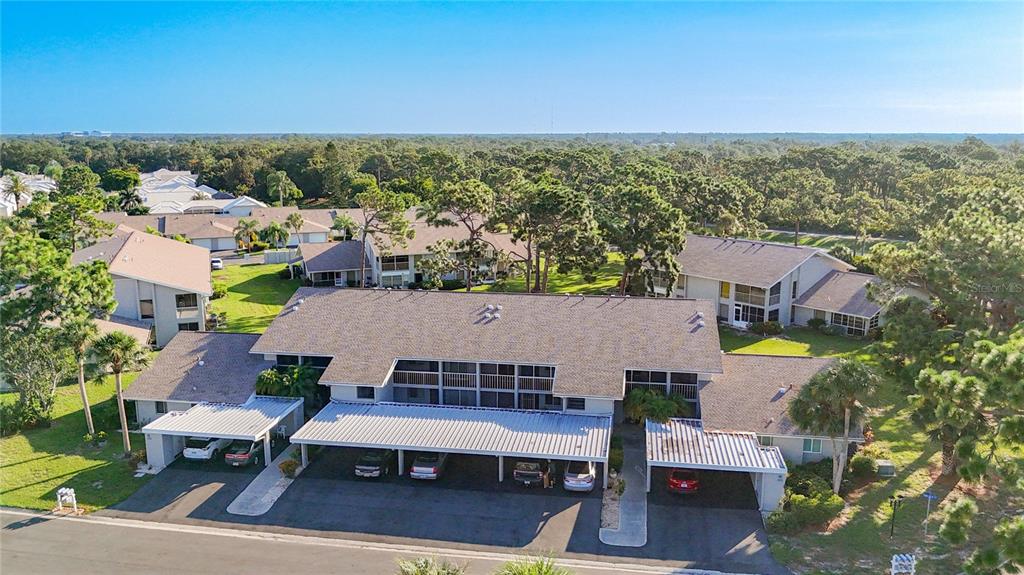 An aerial view of a multi-unit residential building with covered parking and surrounding trees — 1407 PINE LAKE DRIVE UNIT 7, VENICE, FL