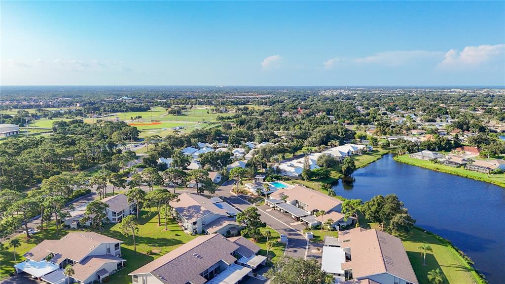 An aerial view shows a residential complex with multiple buildings, a lake, and surrounding trees — 1407 PINE LAKE DRIVE UNIT 7, VENICE, FL