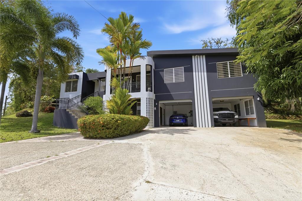 A two-story house with a dark exterior, two garage bays, and a curved white balcony — 1 SECTOR LOS CRUZADOS, MAYAGUEZ, PR