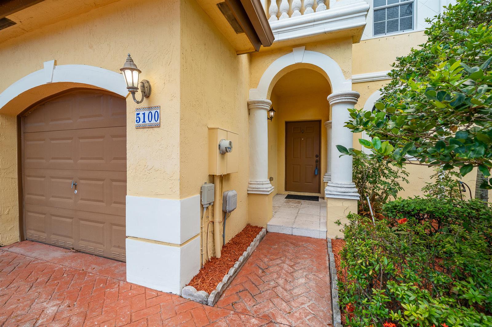 The exterior of a yellow house features a brown garage door, arched entryway, and walkway — 5100 SW 141st Avenue, Miramar FL 33027, MIRAMAR, FL
