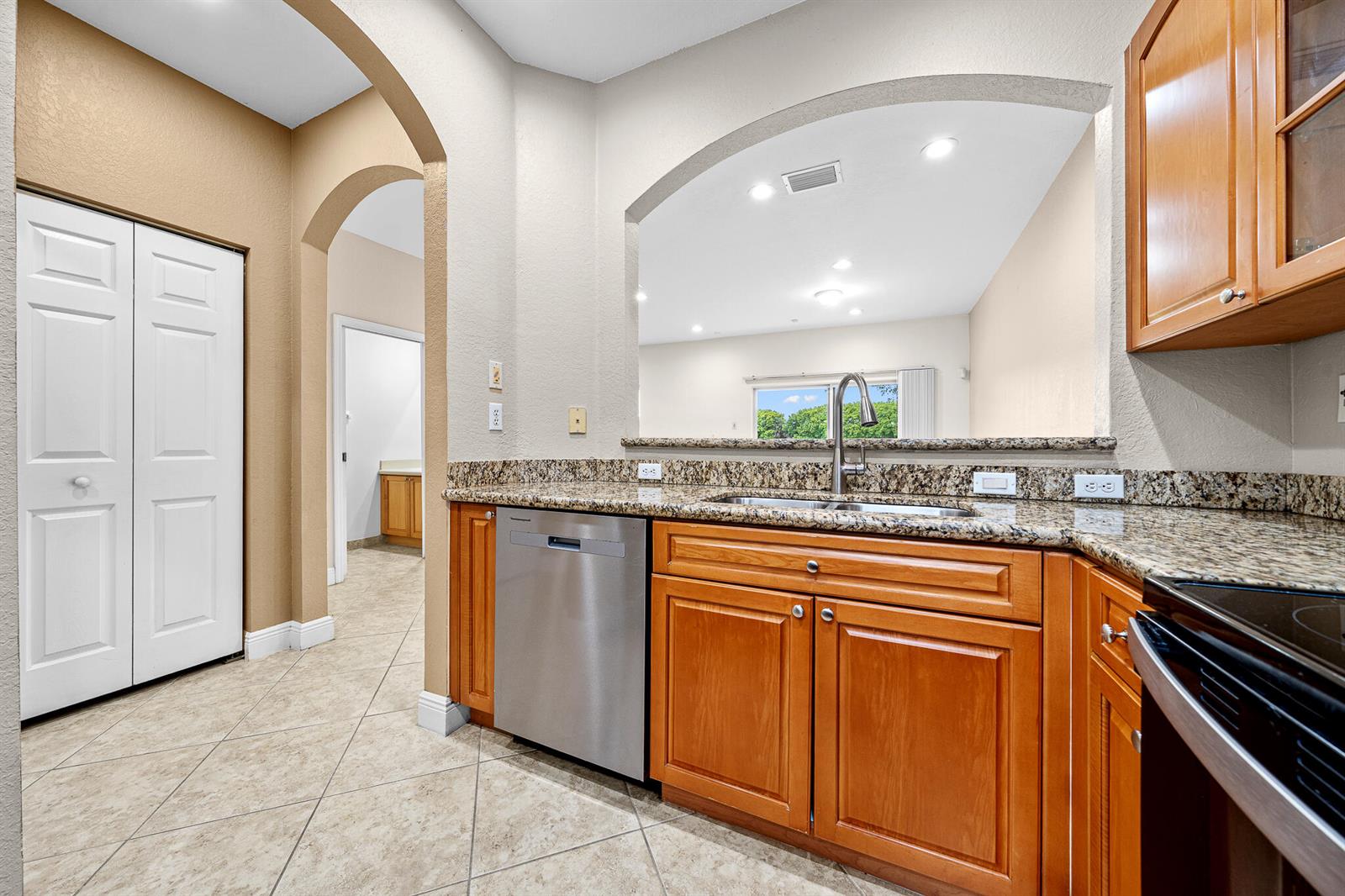 A kitchen features wood cabinets, granite countertops, a stainless steel dishwasher, and a pass-through window — 5100 SW 141st Avenue, Miramar FL 33027, MIRAMAR, FL