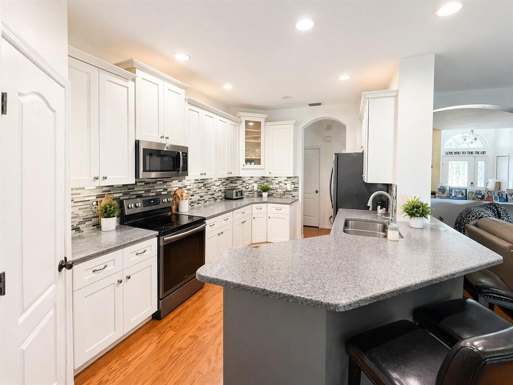 A kitchen features white cabinets, gray granite countertops, stainless steel appliances, and a breakfast bar — 1314 EMERALD HILL WAY, VALRICO, FL