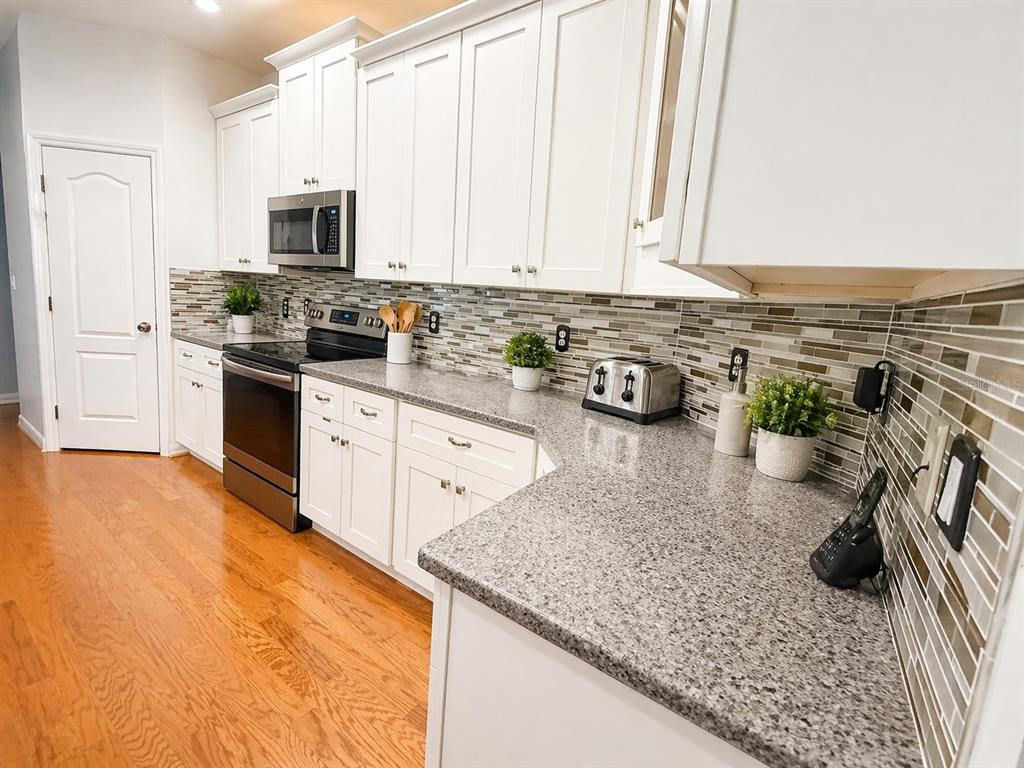 A kitchen features white cabinets, granite countertops, a tiled backsplash, and stainless steel appliances — 1314 EMERALD HILL WAY, VALRICO, FL