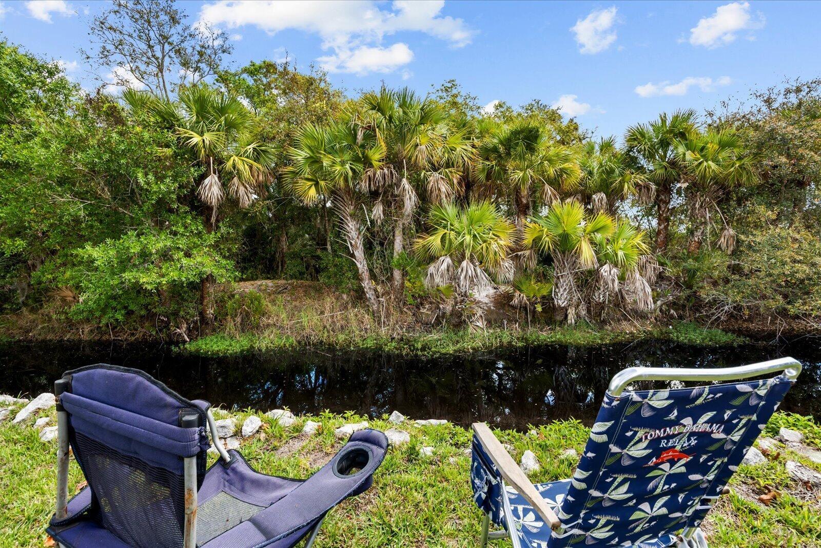 Two folding chairs sit on a grassy bank overlooking a narrow canal and palm trees — 324 Mockingbird Avenue, Fort Pierce FL 34982, FORT PIERCE, FL