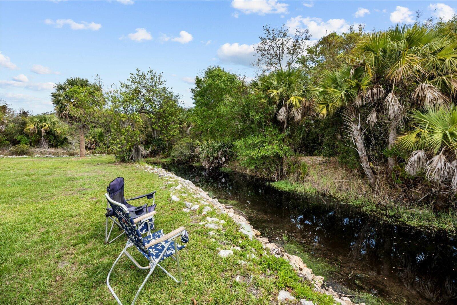 A folding chair sits on a grassy lawn beside a small canal lined with rocks — 324 Mockingbird Avenue, Fort Pierce FL 34982, FORT PIERCE, FL