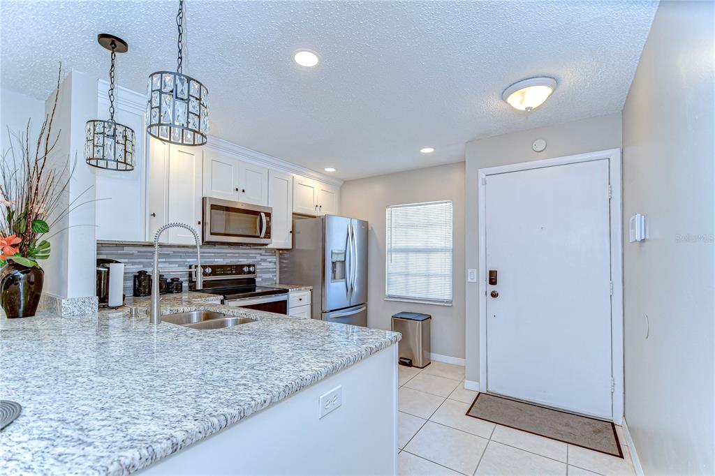 A kitchen with white cabinets, granite countertops, stainless steel appliances, and a white entry door — 13870 OAKWOOD LANE, SEMINOLE, FL