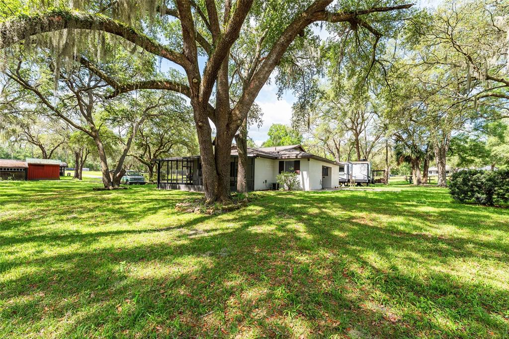 A white house with a screened porch sits on a large, tree-shaded grassy lot — 10871 SE COUNTY ROAD 336, MORRISTON, FL