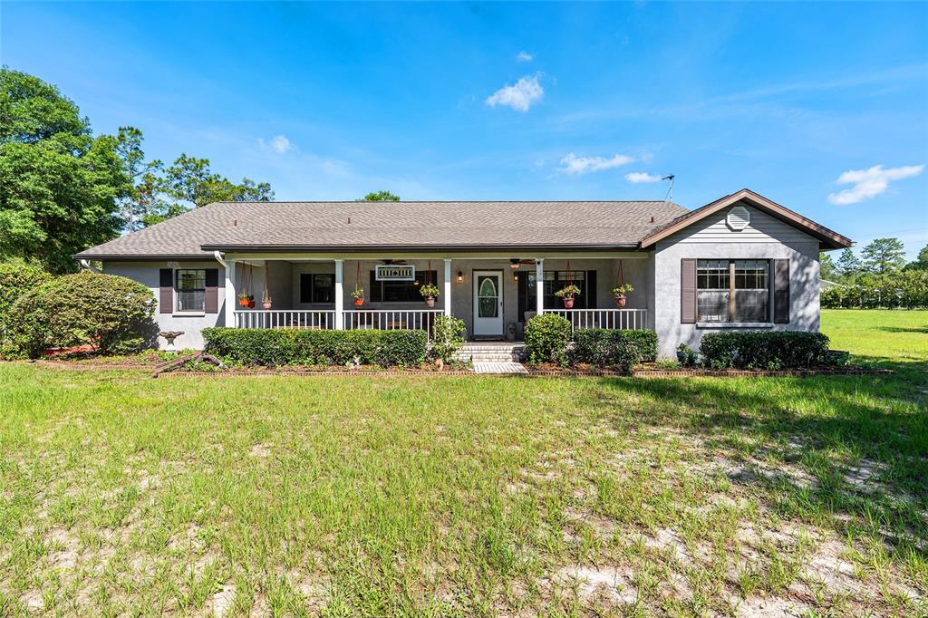 A single-story house with a covered front porch, gray siding, and a large grassy yard — 10871 SE COUNTY ROAD 336, MORRISTON, FL
