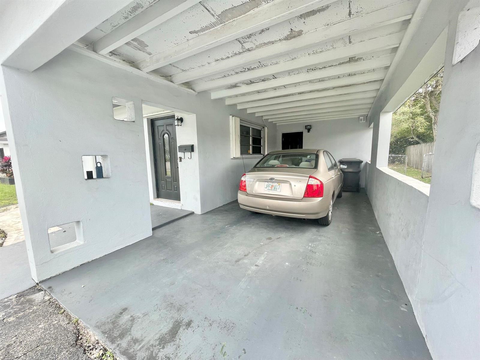 A covered carport with a concrete floor leads to a front door and a parked car — 5630 Hollywood Boulevard, Hollywood FL 33021, HOLLYWOOD, FL