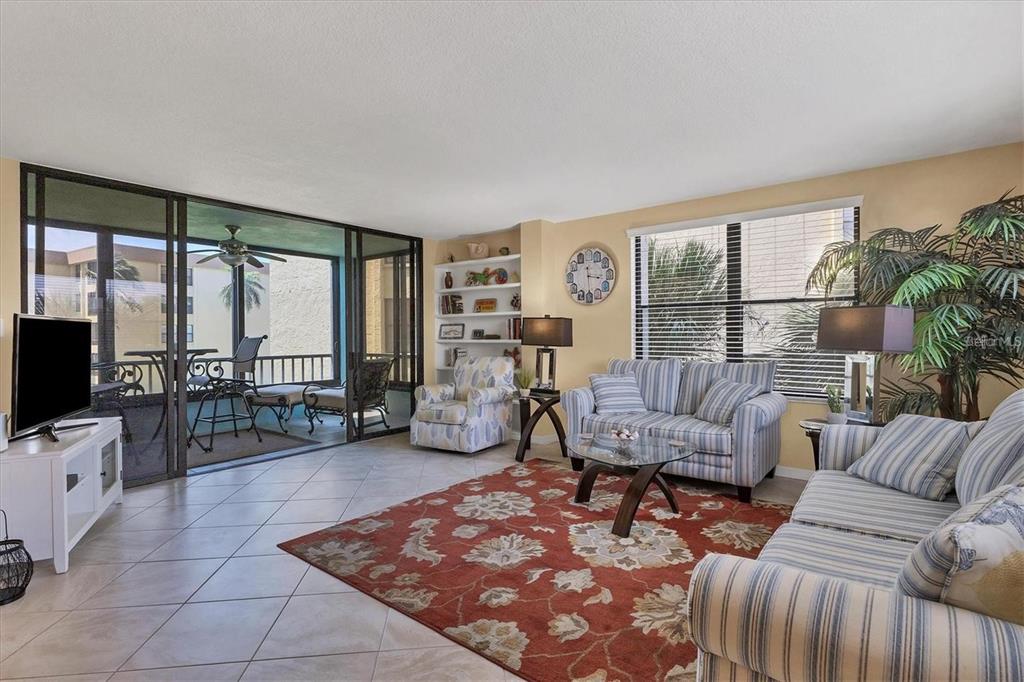 A living room features striped sofas, a patterned rug, built-in shelving, and a screened balcony — 8776 MIDNIGHT PASS ROAD UNIT C307, SARASOTA, FL