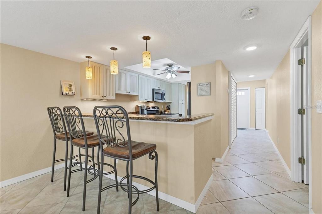 A kitchen features a breakfast bar with three metal stools, light cabinetry, and tiled floors — 8776 MIDNIGHT PASS ROAD UNIT C307, SARASOTA, FL