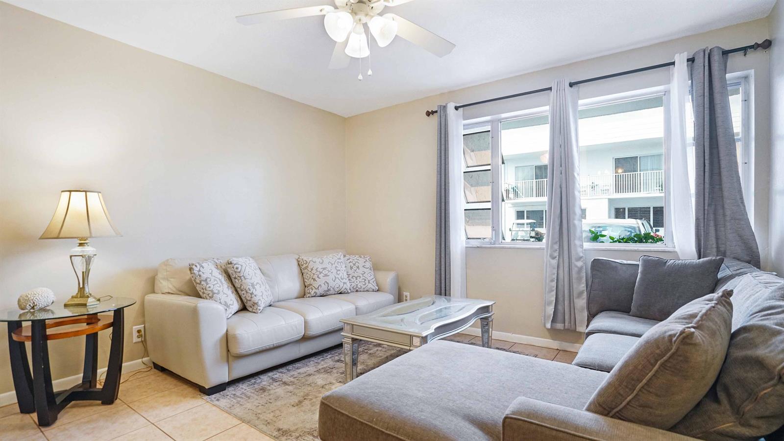 A living room features a beige sofa, a grey sectional, and a glass coffee table — 412 S Cypress Road # 205, Pompano Beach FL 33060, POMPANO BEACH, FL