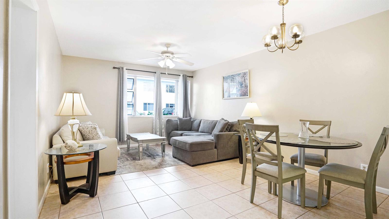 This living and dining area features tile flooring, a gray sectional sofa, and a chandelier — 412 S Cypress Road # 205, Pompano Beach FL 33060, POMPANO BEACH, FL