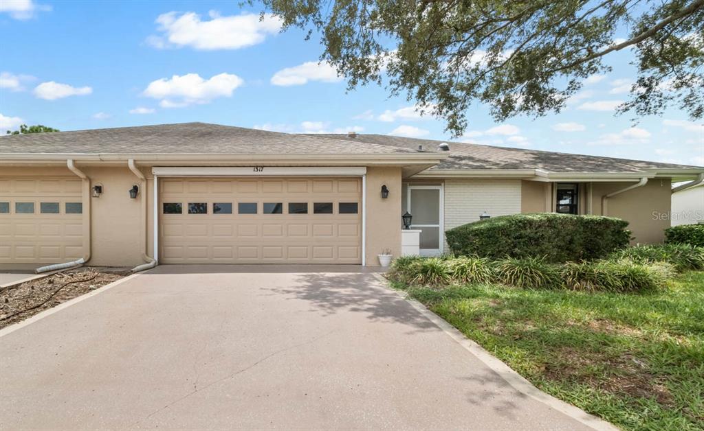 A single-story attached home features a beige stucco exterior, a two-car garage, and a driveway — 1317 LELAND DRIVE, SUN CITY CENTER, FL