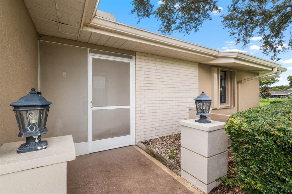 A concrete walkway leads to a screened front door flanked by two outdoor pedestal lanterns — 1317 LELAND DRIVE, SUN CITY CENTER, FL