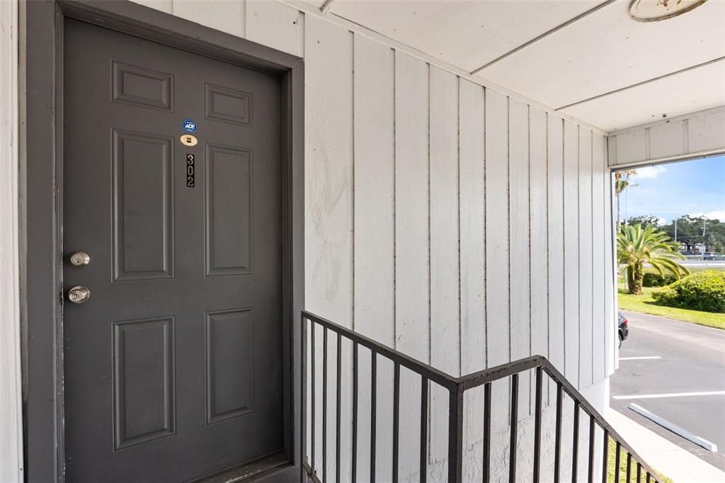A dark gray door with the number 302 is located at the top of outdoor stairs — 1000 S SEMORAN BOULEVARD UNIT 302, WINTER PARK, FL
