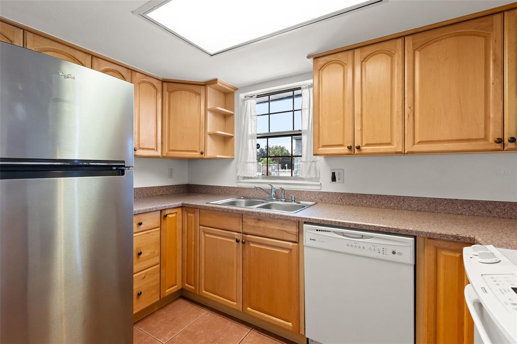 A kitchen features light wood cabinets, a stainless steel refrigerator, a dishwasher, and tile flooring — 1000 S SEMORAN BOULEVARD UNIT 302, WINTER PARK, FL