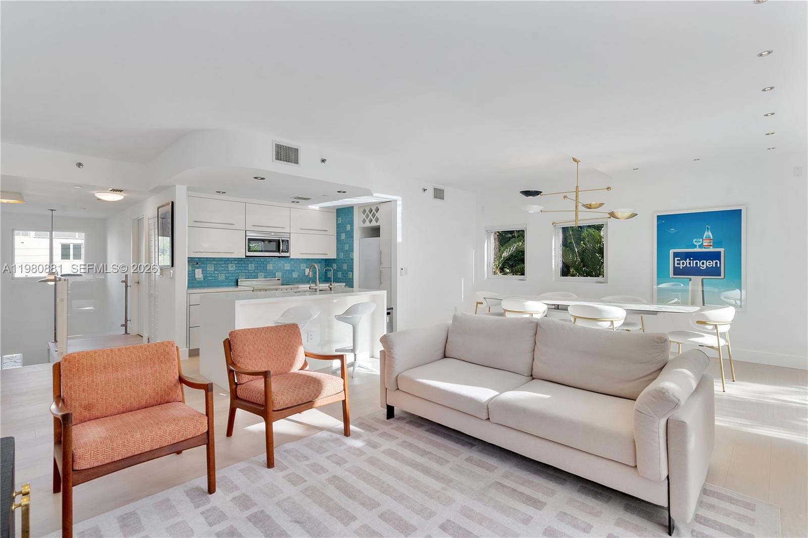 An open-concept living and dining area features white cabinetry, a blue backsplash, and modern furniture — 828 3rd St # 314, Miami Beach FL 33139, MIAMI BEACH, FL
