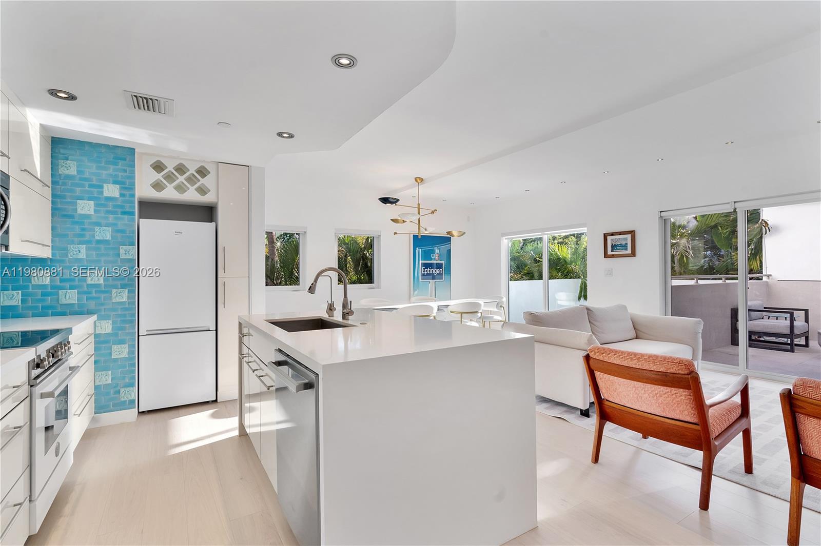 A modern open-concept kitchen and living area features a white island, blue tile, and balcony — 828 3rd St # 314, Miami Beach FL 33139, MIAMI BEACH, FL