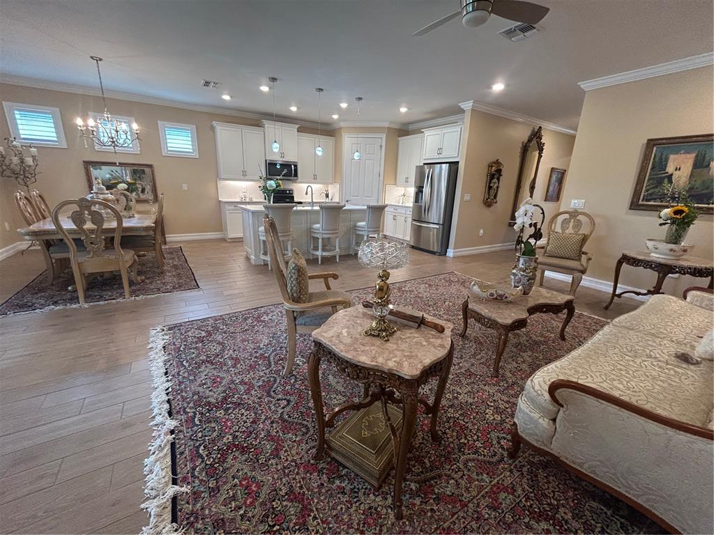 An open-concept kitchen and living area features light wood flooring, white cabinetry, and traditional furniture — 126 VILLA PEROSA WAY, NOKOMIS, FL
