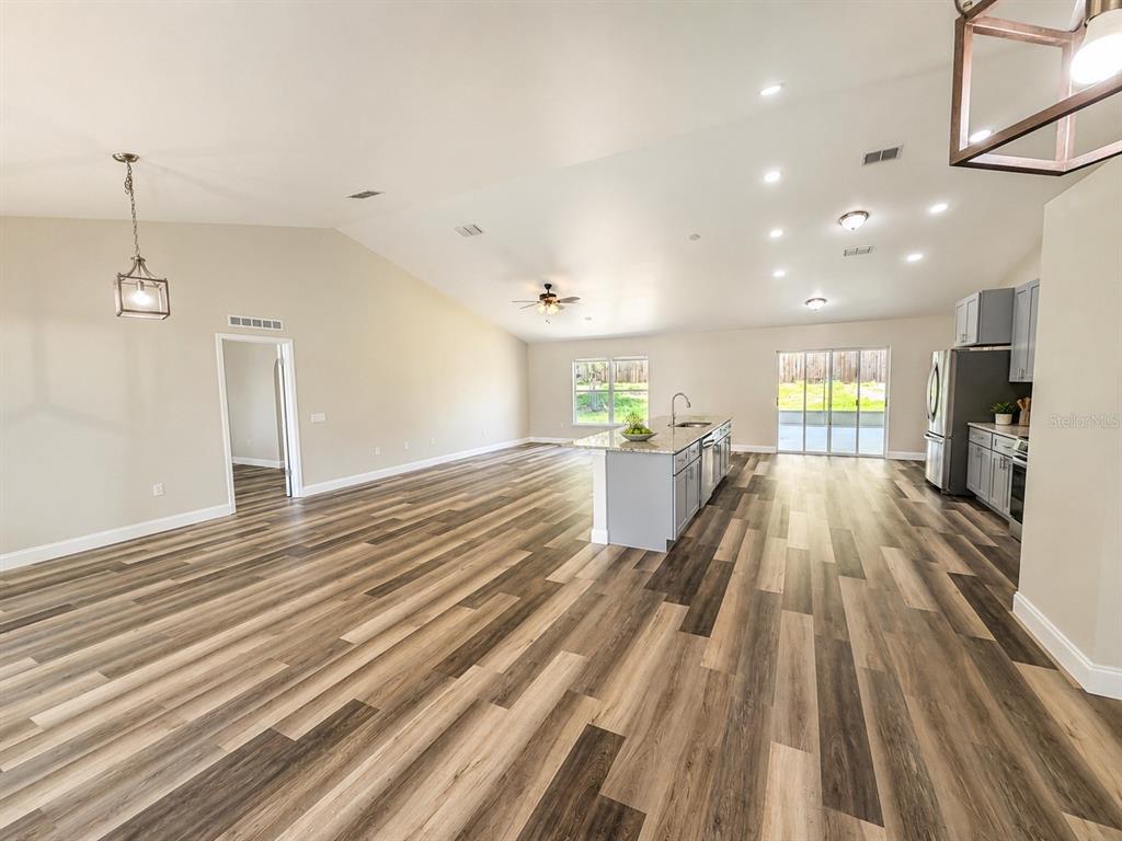 An open-concept kitchen and living area features vaulted ceilings, wood-look flooring, and a center island — 3228 WHITE BLOSSOM LANE, CLERMONT, FL