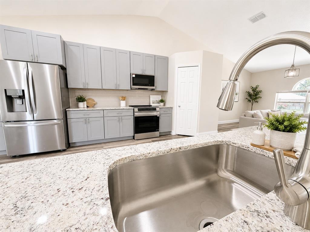 A kitchen features light gray cabinets, stainless steel appliances, and a granite-topped island — 3228 WHITE BLOSSOM LANE, CLERMONT, FL