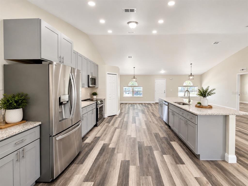 A modern kitchen features gray cabinets, stainless steel appliances, and a large granite-topped island — 3228 WHITE BLOSSOM LANE, CLERMONT, FL