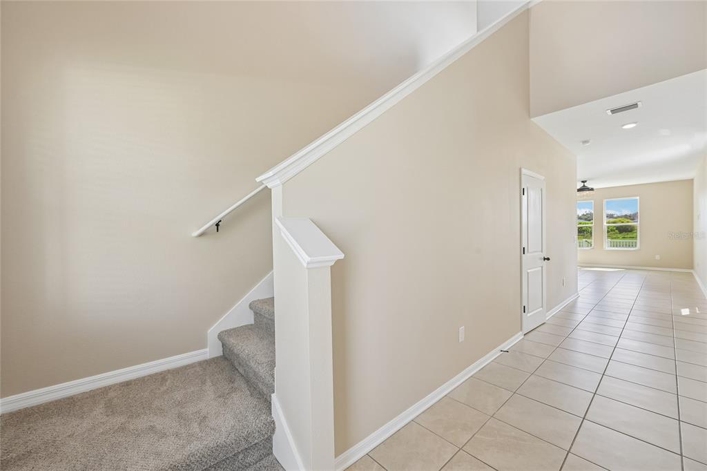 A carpeted staircase with a white railing sits beside a tiled hallway and doorway — 4702 BIRDSONG DRIVE, PALMETTO, FL