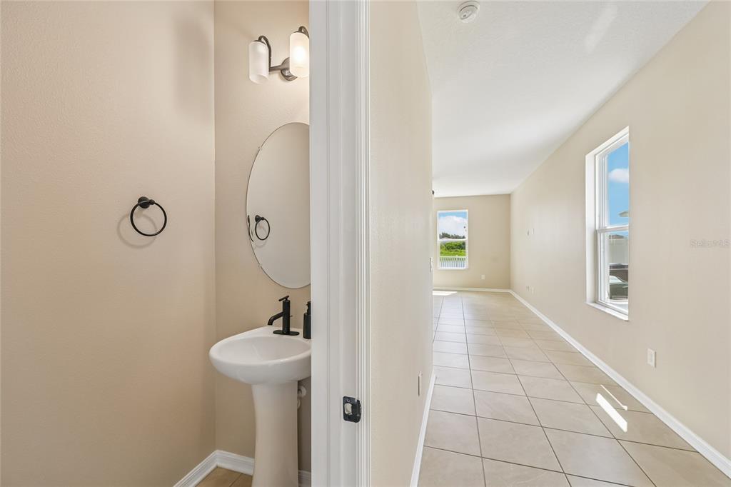 A small powder room with a pedestal sink sits beside a tiled hallway — 4702 BIRDSONG DRIVE, PALMETTO, FL