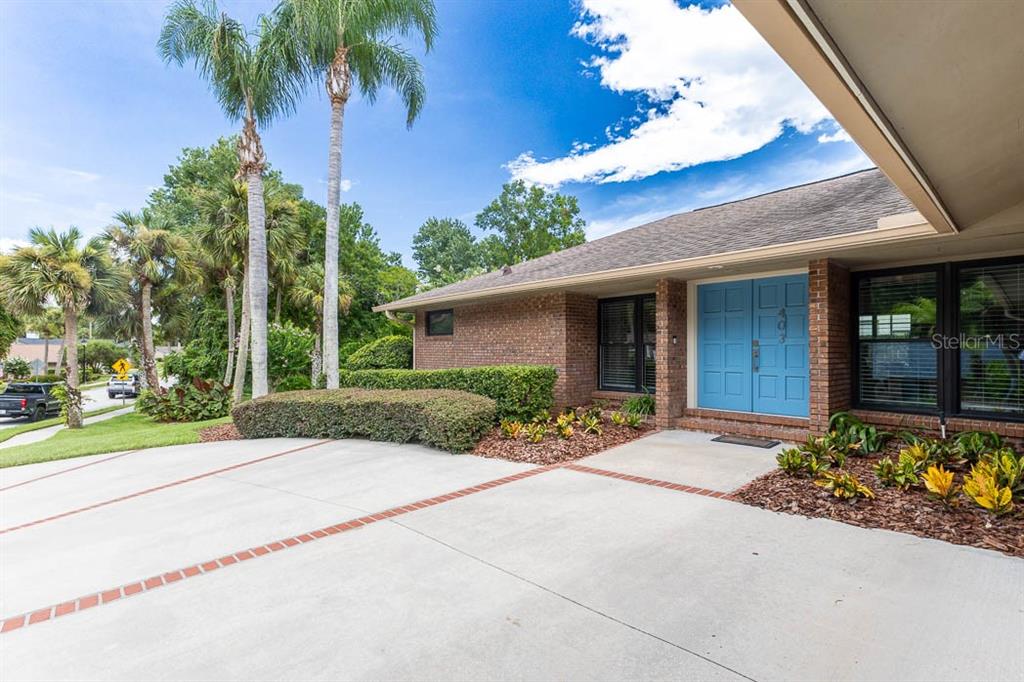 A brick house exterior features a blue double front door and a concrete driveway — 403 TIMBER RIDGE DRIVE, LONGWOOD, FL