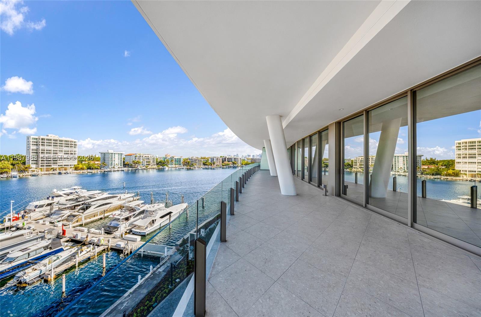 A spacious balcony with glass railings overlooks a marina filled with yachts and city buildings — 5 Grove Isle Dr # 504, Coconut Grove FL 33133, COCONUT GROVE, FL