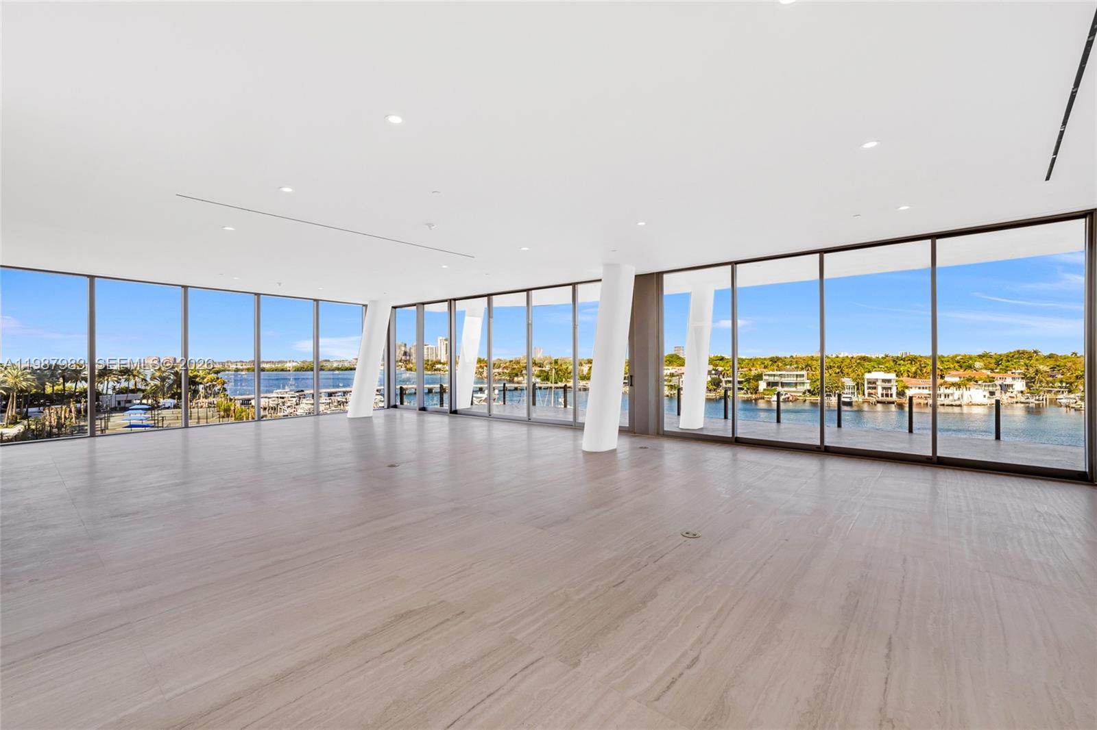 An expansive, empty room features floor-to-ceiling windows, white support columns, and light-colored stone flooring — 5 Grove Isle Dr # 504, Coconut Grove FL 33133, COCONUT GROVE, FL