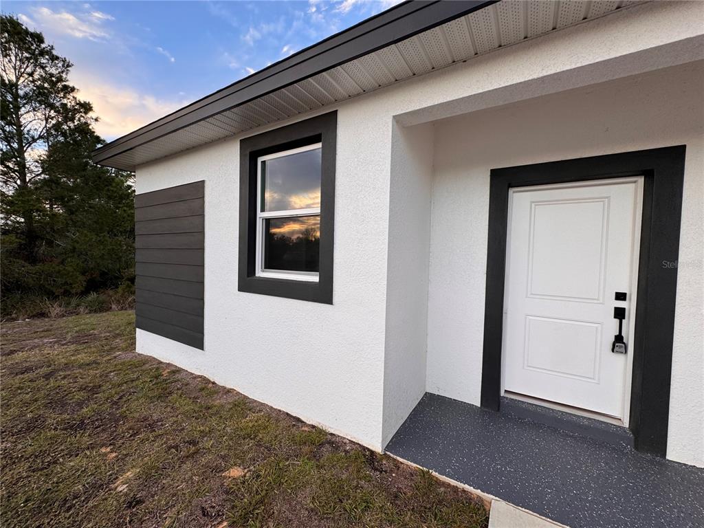 A white stucco house exterior features a dark-trimmed window, a white front door, and siding — 1940 ALAN STREET, SEBRING, FL
