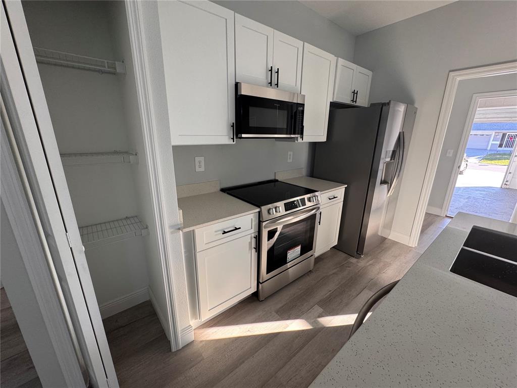 A kitchen features white cabinets, stainless steel appliances, light countertops, and wood-look flooring — 1940 ALAN STREET, SEBRING, FL