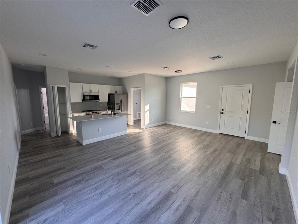 An open-concept kitchen and living area features light gray walls and wood-look plank flooring — 1940 ALAN STREET, SEBRING, FL
