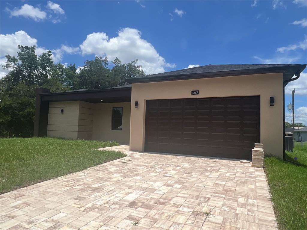 A single-story house features a tan stucco exterior, a dark brown garage door, and a paver driveway — 21492 DOLLARD AVENUE, PORT CHARLOTTE, FL