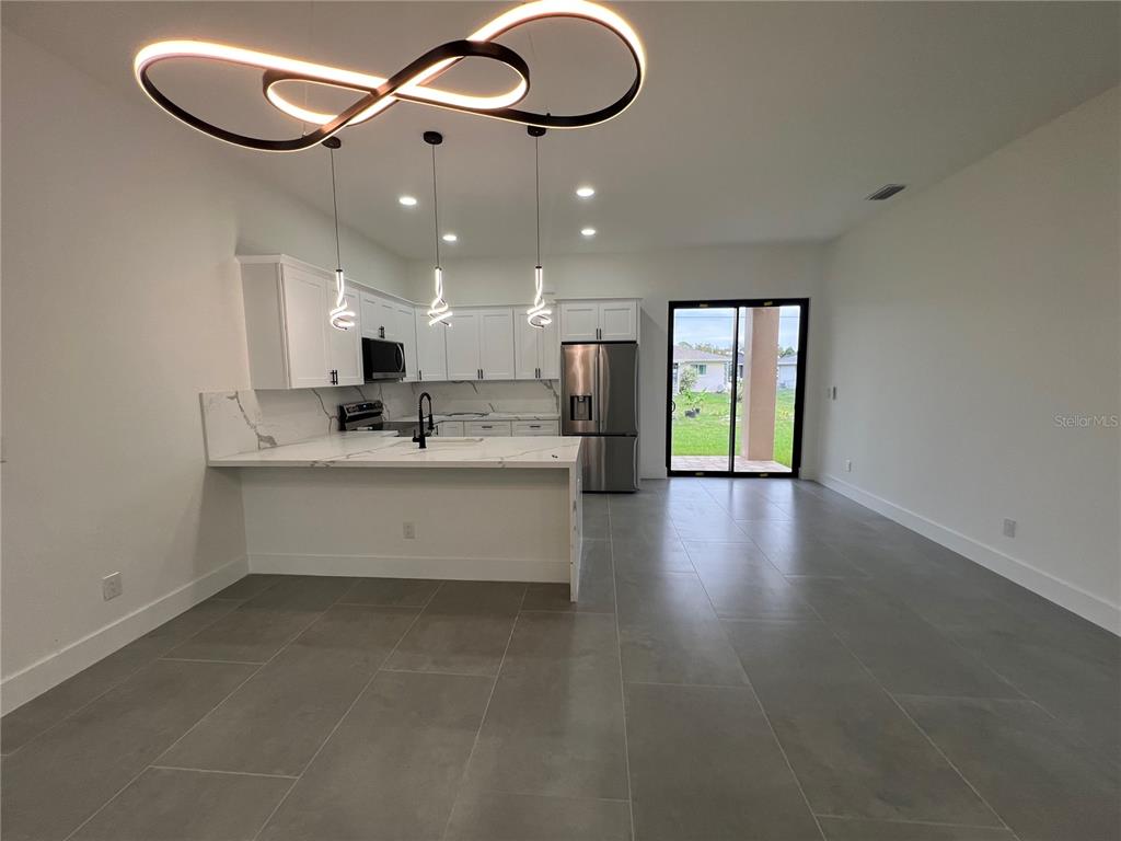 A modern kitchen features white cabinetry, marble-look countertops, stainless steel appliances, and gray tile flooring — 21492 DOLLARD AVENUE, PORT CHARLOTTE, FL