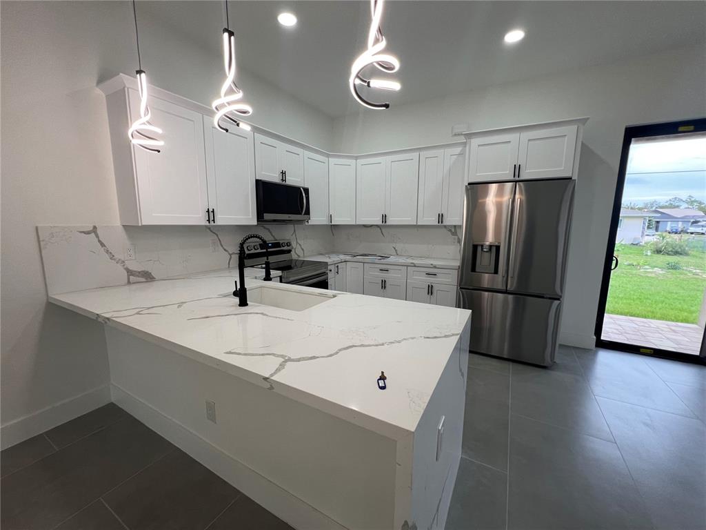 A modern kitchen features white cabinets, marble-look countertops, stainless steel appliances, and pendant lighting — 21492 DOLLARD AVENUE, PORT CHARLOTTE, FL
