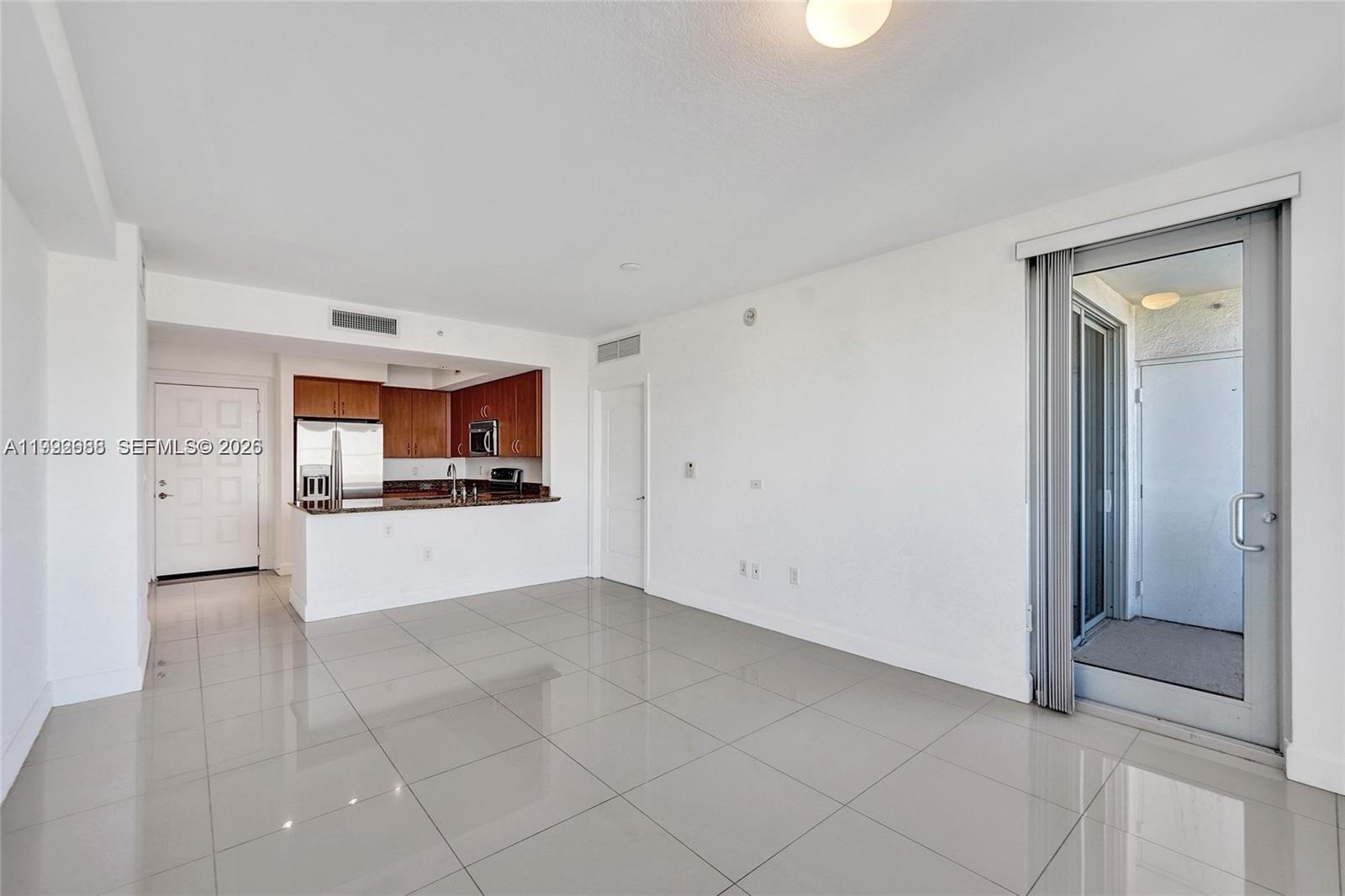 An open-concept living area features light tile flooring, a kitchen with wood cabinets, and a balcony — 1830 Radius Dr # 609, Hollywood FL 33020, HOLLYWOOD, FL