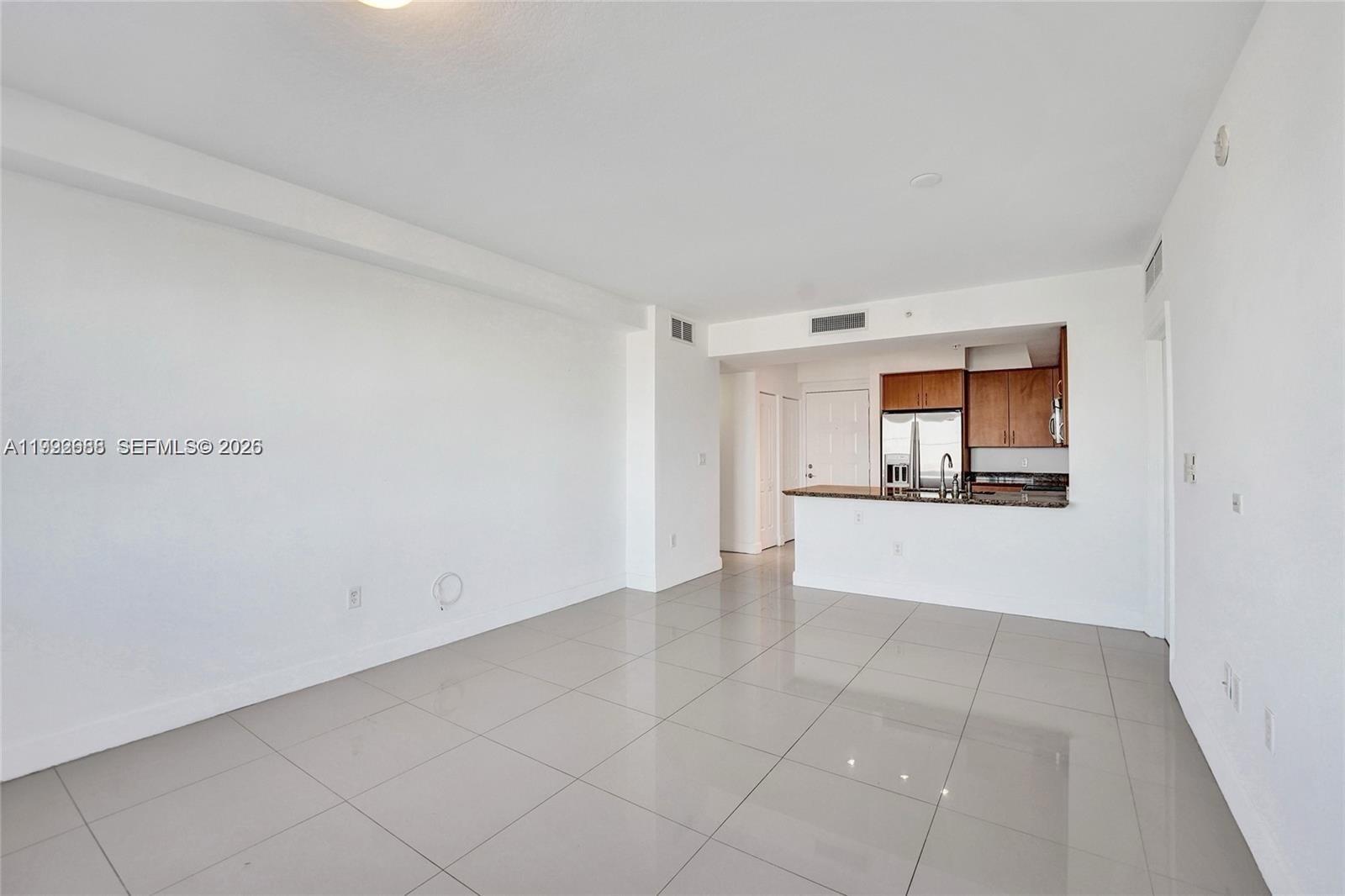 An unfurnished living room with white walls, light tile flooring, and an open kitchen — 1830 Radius Dr # 609, Hollywood FL 33020, HOLLYWOOD, FL