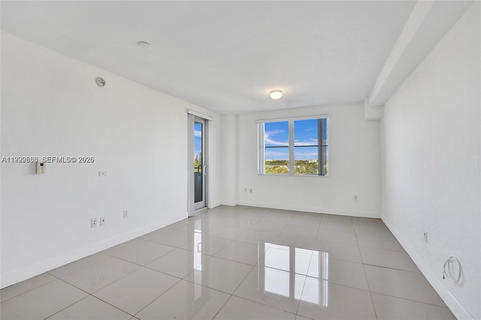 An empty room features white walls, light-colored tile flooring, a window, and a glass door — 1830 Radius Dr # 609, Hollywood FL 33020, HOLLYWOOD, FL