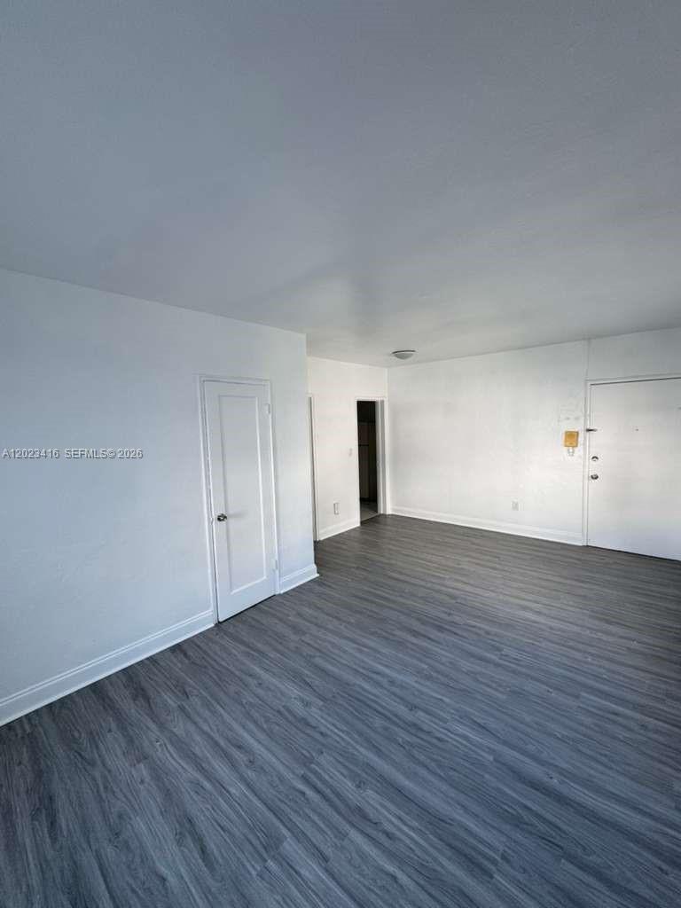 An empty room features white walls, a white door, and grey wood-look flooring — MIAMI BEACH, FL