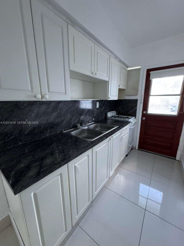 A kitchen features white cabinets, a dark marble-patterned countertop, and a stainless steel sink — MIAMI BEACH, FL