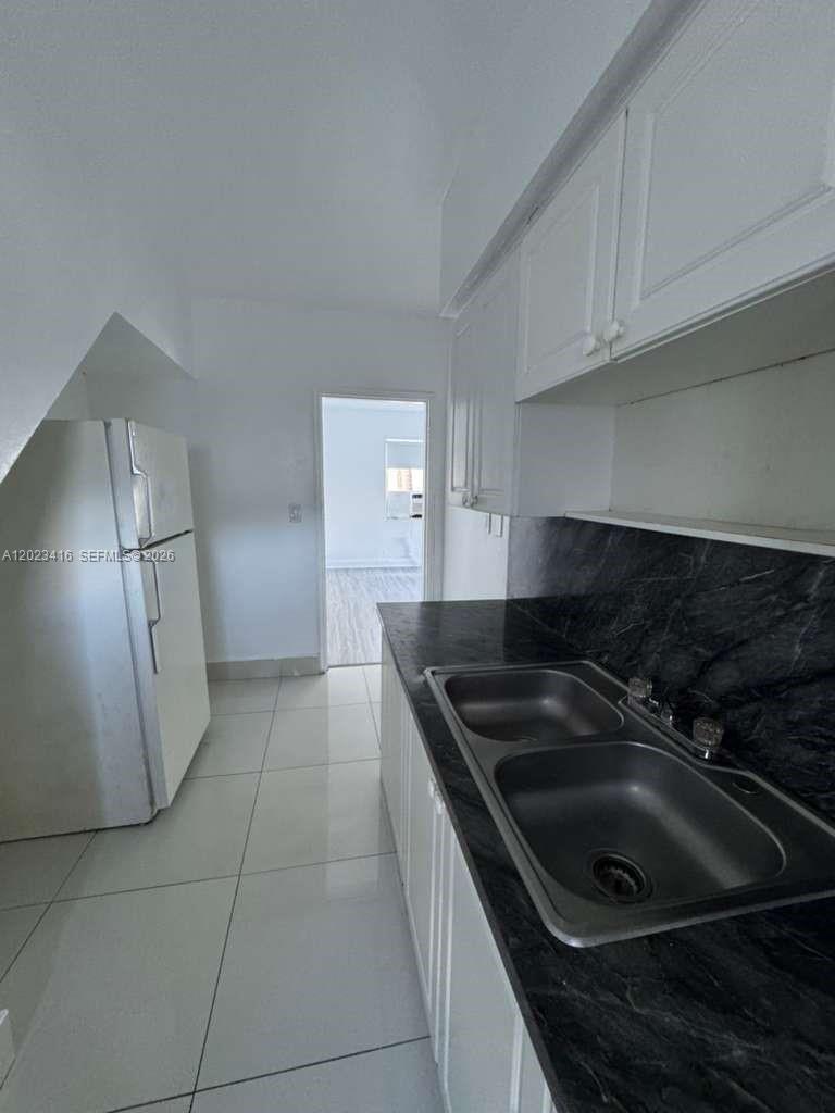 A kitchen features white cabinets, a dark marble-patterned countertop, a double sink, and white appliances — MIAMI BEACH, FL
