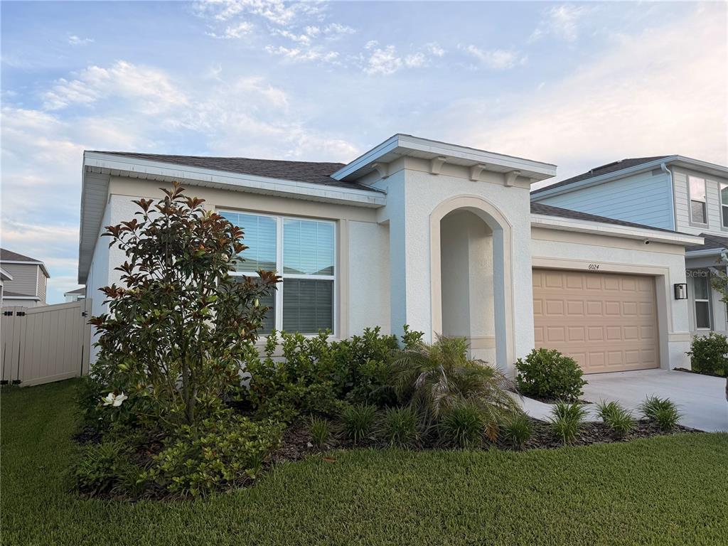A single-story house with a white stucco exterior, a tan garage door, and front landscaping — 6024 FOREST PERCH DRIVE, ST CLOUD, FL
