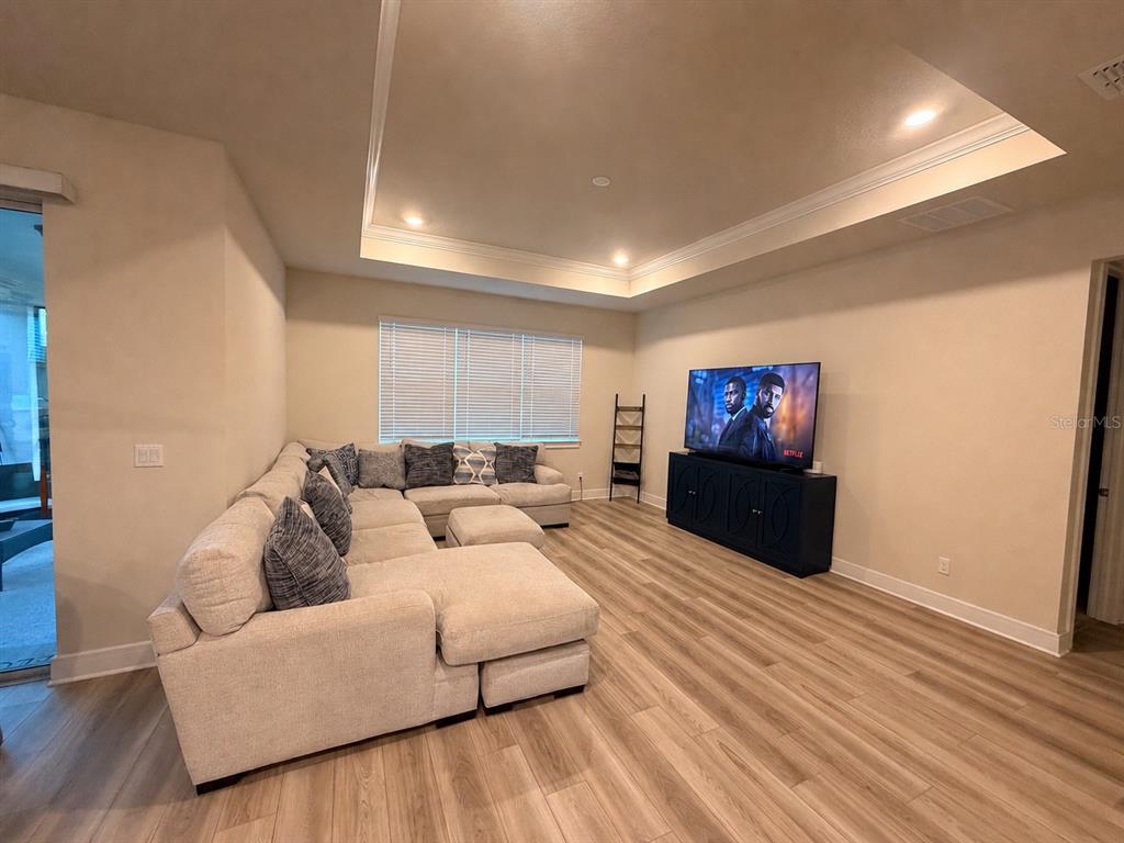 A living room features a large sectional sofa, a television on a console, and wood-look flooring — 6024 FOREST PERCH DRIVE, ST CLOUD, FL