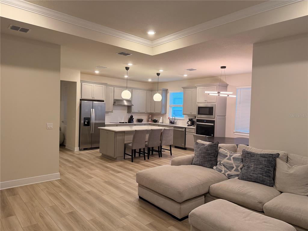 An open-concept kitchen with a central island and stainless steel appliances overlooks a living area — 6024 FOREST PERCH DRIVE, ST CLOUD, FL